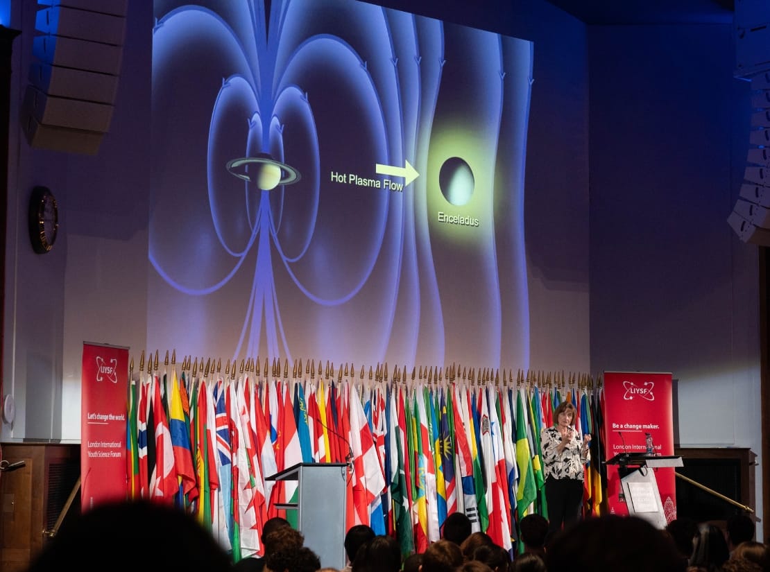 Speaker presenting at LIYSF with international participants and global flags backdrop