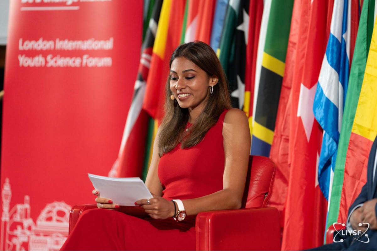 LIYSF student speaker presenting during an international science forum session surrounded by national flags
